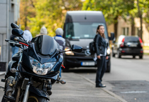 A motorcycle parked on a sidewalk, with a person in the background about to cross the street.